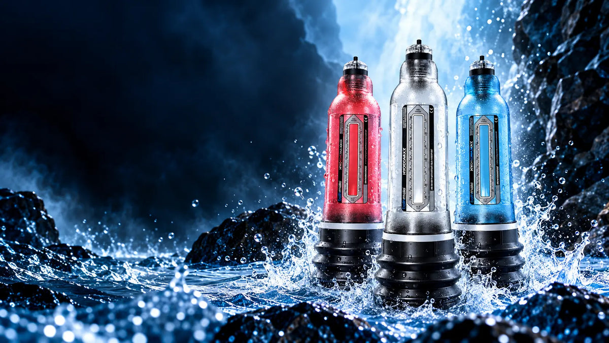 Three Bathmate Hydromax pumps standing upright in splashing water among dark rocks, with one red, one clear, and one blue device in the center.